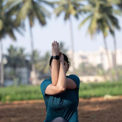 Seated forward bow with hands pressed together overhead, palm trees behind